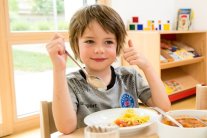 Junge in einer Kita am Essen mit Daumen nach oben